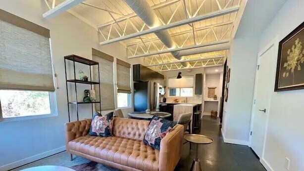 A modern living room with a leather sofa, glass coffee table, and a dining area with a kitchen in the background.