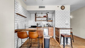 Una cocina compacta con azulejos blancos tipo metro, taburetes de bar de madera y una pequeña isla.