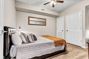 A bedroom with a bed, a ceiling fan, a door, and a mirror on the wall.