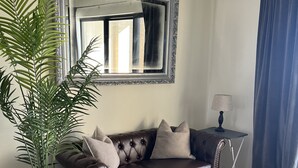 Una sala de estar con un sofá de cuero marrón, una mesa de centro, una planta en maceta, un espejo, una lámpara y una cortina azul.