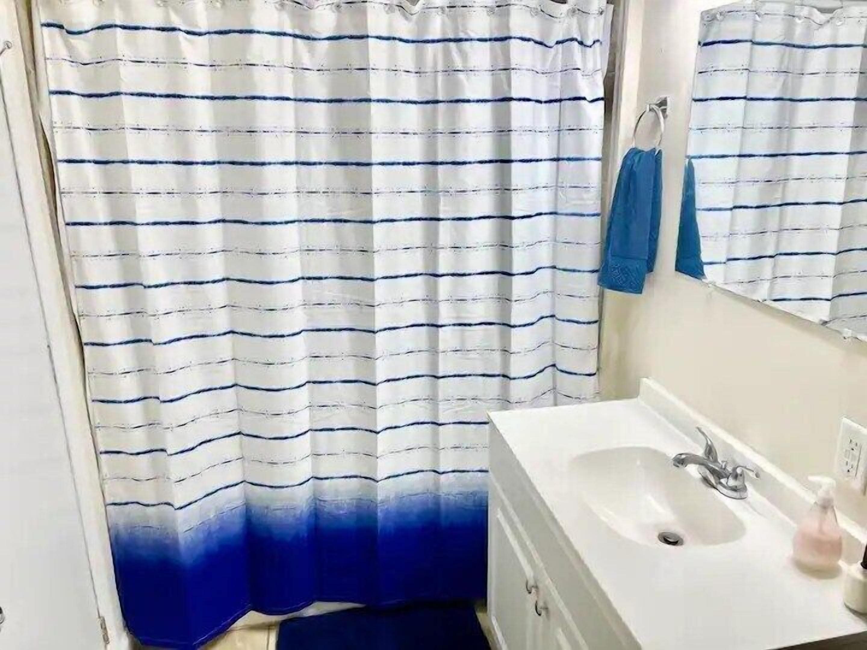Un baño con un lavamanos blanco, un espejo y una cortina de ducha azul y blanca a rayas.