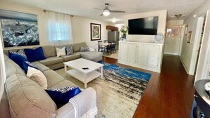 Una sala de estar con un sofá, una mesa de centro y un televisor. Hay un comedor con sillas y una mesa.