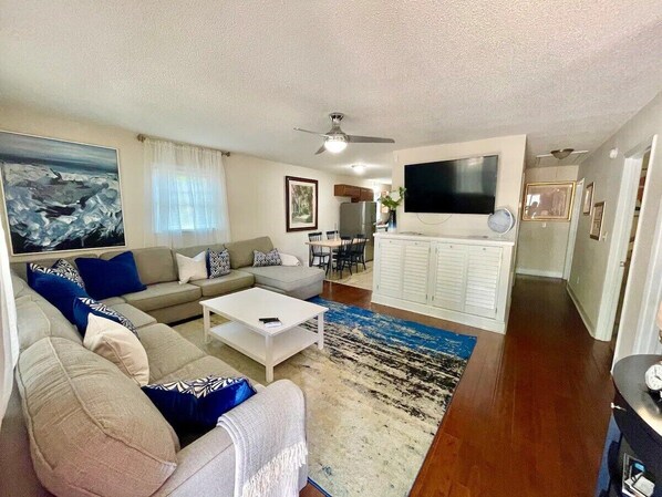 A living room with a sofa, coffee table, and a TV. There is a dining area with chairs and a table.