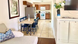 Un espacio habitable compacto con comedor, kitchenette y televisor en la pared.