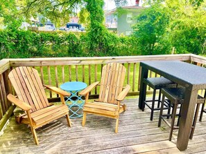 A wooden deck with two Adirondack chairs and a small round table.