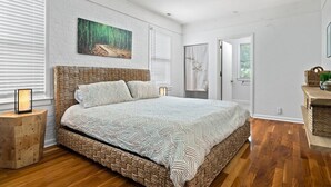 A bedroom with a woven headboard, a patterned bedspread, a framed picture on the wall, and a nightstand with a lamp. - Rising Sun Retreat - 4 Miles to Beach (Wilmington)