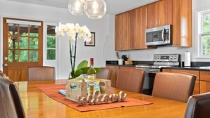 A modern kitchen with wooden cabinets, stainless steel appliances, and a dining area with a wooden table and leather chairs. - Rising Sun Retreat - 4 Miles to Beach (Wilmington)
