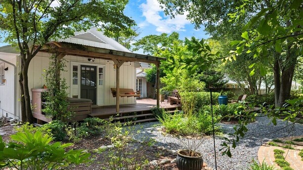 A covered outdoor seating area with a wooden bench and a table, surrounded by lush greenery and a gravel path. - Rising Sun Retreat - 4 Miles to Beach (Wilmington)