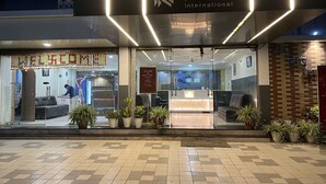 Exterior del Hotel Niraj International, con mostrador de recepción, plantas en macetas y un mostrador de registro.