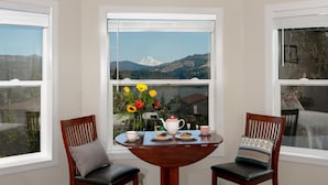 Un coin repas avec une table dressée pour deux personnes, un vase de fleurs et une vue sur une montagne.
