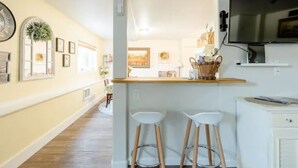 Une cuisine avec un plan de travail en bois, deux tabourets de bar blancs, un téléviseur fixé au mur et un panier posé sur le plan de travail.