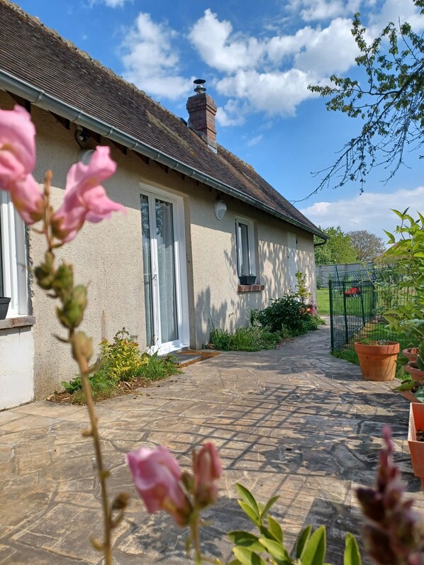 A house with a stone pathway leading to the entrance, surrounded by greenery and a fenced garden.