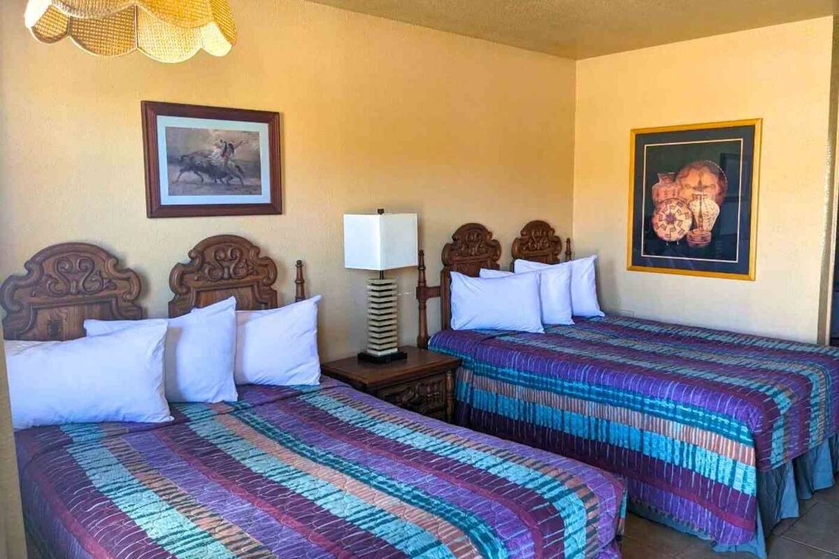 A hotel room with two double beds, a bedside table with a lamp, and two framed pictures on the walls.