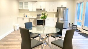A modern kitchen with white cabinets, stainless steel appliances, and a glass dining table with four chairs. - Brand New Walk Out Bsmt Apt Near Beach  (Pickering)