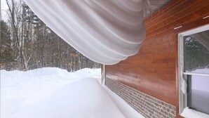 Una cabaña de madera con porche cubierto, fachada de ladrillo y terreno cubierto de nieve.