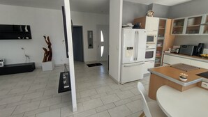 Une cuisine moderne avec des appareils électroménagers blancs, un coin repas avec une table et des chaises blanches, et un couloir avec une porte blanche.