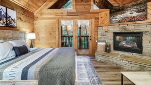 A log cabin bedroom with a bed, a stone fireplace, and a view of the outdoors. - 10 Min to Gatlinburg Strip Hot Tub King Bed Pool, 5 min to Rocky Top Sport World (Gatlinburg)