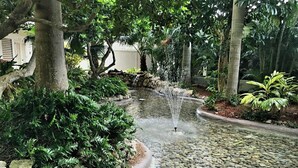 Un jardín tranquilo con una fuente de agua, rodeado de exuberante follaje y un sendero de piedra.