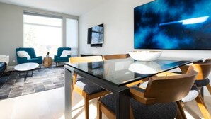 A modern dining area with a glass table, blue chairs, and a large abstract painting on the wall. - Capitol Hill Townhouse with Private Rooftop Deck — Space Needle & Skyline Views (Seattle)
