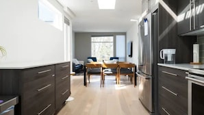 A modern kitchen with dark cabinetry, a stainless steel refrigerator, and a dining area with a wooden table and chairs. - Capitol Hill Townhouse with Private Rooftop Deck — Space Needle & Skyline Views (Seattle)