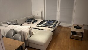 Un ambiente compatto con divano, un letto con coperta fantasia, un tavolino e un termosifone.