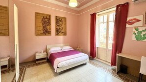 Ein Schlafzimmer mit Bett, Nachttischen, einem Spiegel, einem Fenster mit Vorhängen und Bildern an den Wänden.