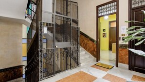 Eine Hotelhalle mit Treppe, einer Rezeption und einer Tür mit schmiedeeisernem Zierwerk.