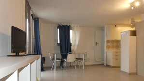 A modern kitchen with white cabinets, a dining area with a glass table and chairs, and a TV on a white counter. - Studio apartment in Isola del Giglio locality Castello (Giglio Castello)