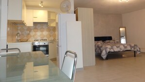 A compact kitchen with a dining table and chairs, a bed with a patterned bedspread, and a ceiling fan. - Studio apartment in Isola del Giglio locality Castello (Giglio Castello)