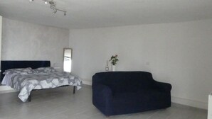 A minimalist bedroom with a bed, a dark sofa, and a small plant. - Studio apartment in Isola del Giglio locality Castello (Giglio Castello)