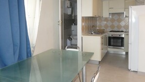A compact kitchen with a glass table, white cabinets, a stove, and a refrigerator. - Studio apartment in Isola del Giglio locality Castello (Giglio Castello)