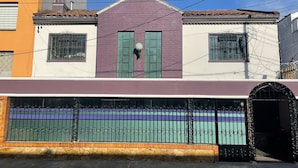 A two-story building with a purple facade, green shutters, and a black gate with a decorative design. - Hotel Casa Morada (Bogotá)