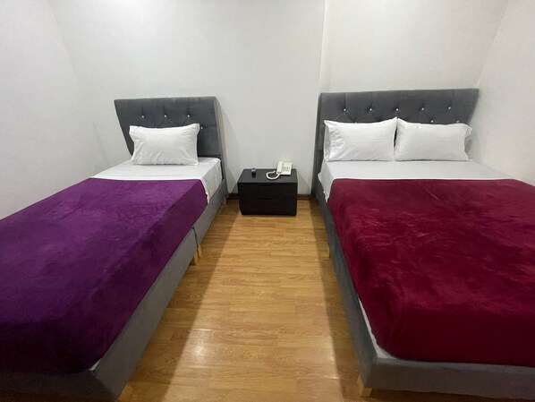 Una habitación con dos camas, cada una con cabecera y almohada. Hay una mesita entre las camas con un teléfono encima.