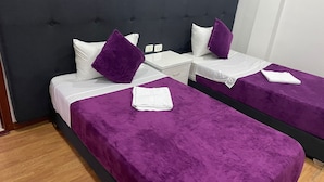 A hotel room with two beds, each with a purple bedspread and white linens. There is a nightstand between the beds with a lamp and a small table. - Hotel Casa Morada (Bogotá)