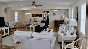 A spacious living room with a white sofa, a black armchair, and a dining area with a table and chairs.