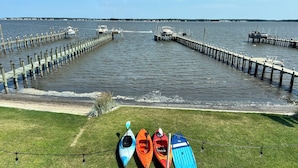 A pier extending into calm water with kayaks lined up on the grass nearby.