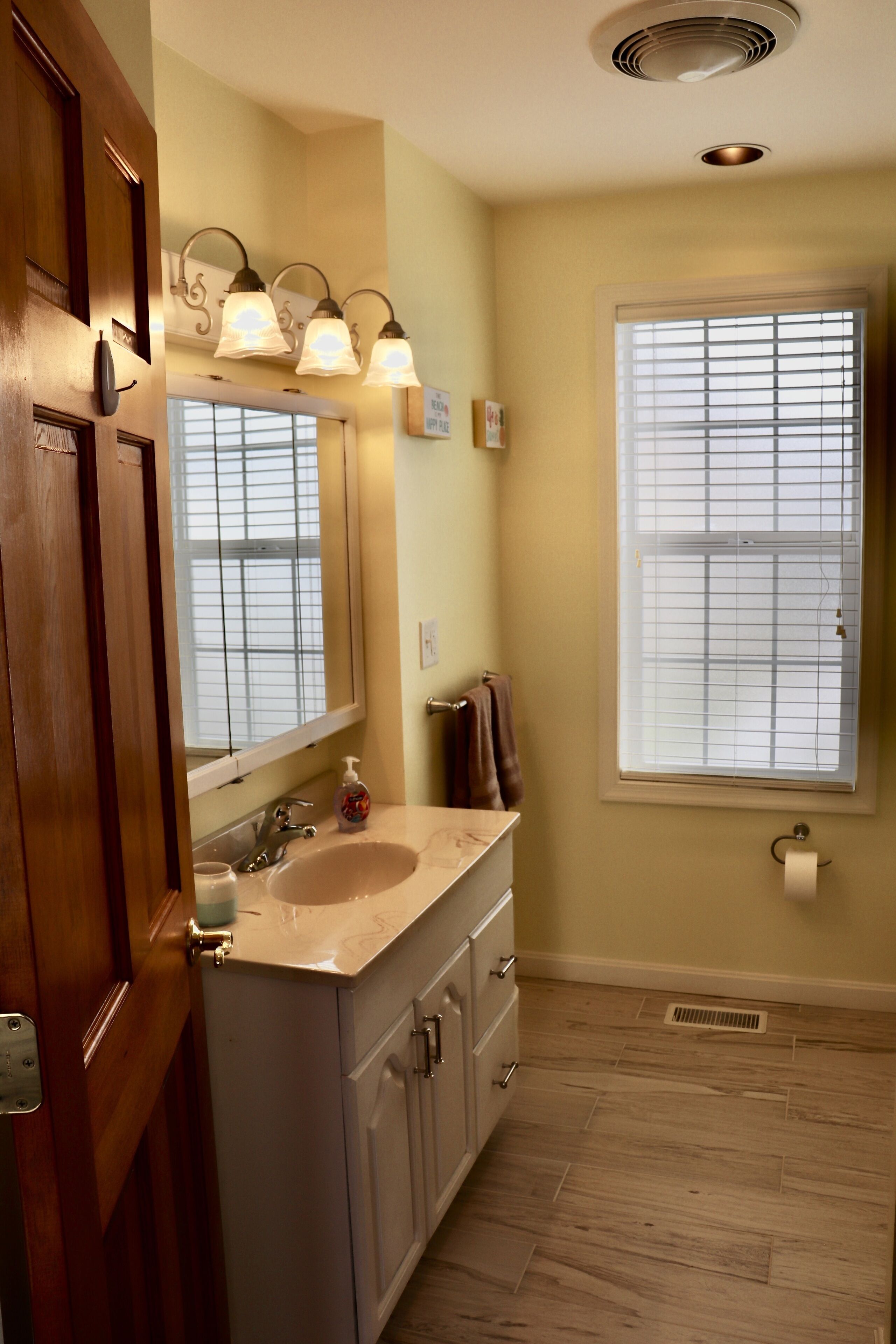 A bathroom with a large vanity, a mirror, a window with blinds, and a wooden door.