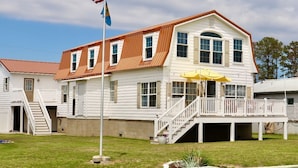 A white two-story house with a brown roof, a front porch, and a flagpole with an American flag.