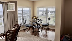 A dining area with a table and chairs, a ceiling fan, and large windows with blinds.