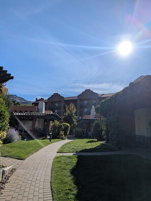 A courtyard with a paved walkway, a building with multiple balconies, and a clear sky.