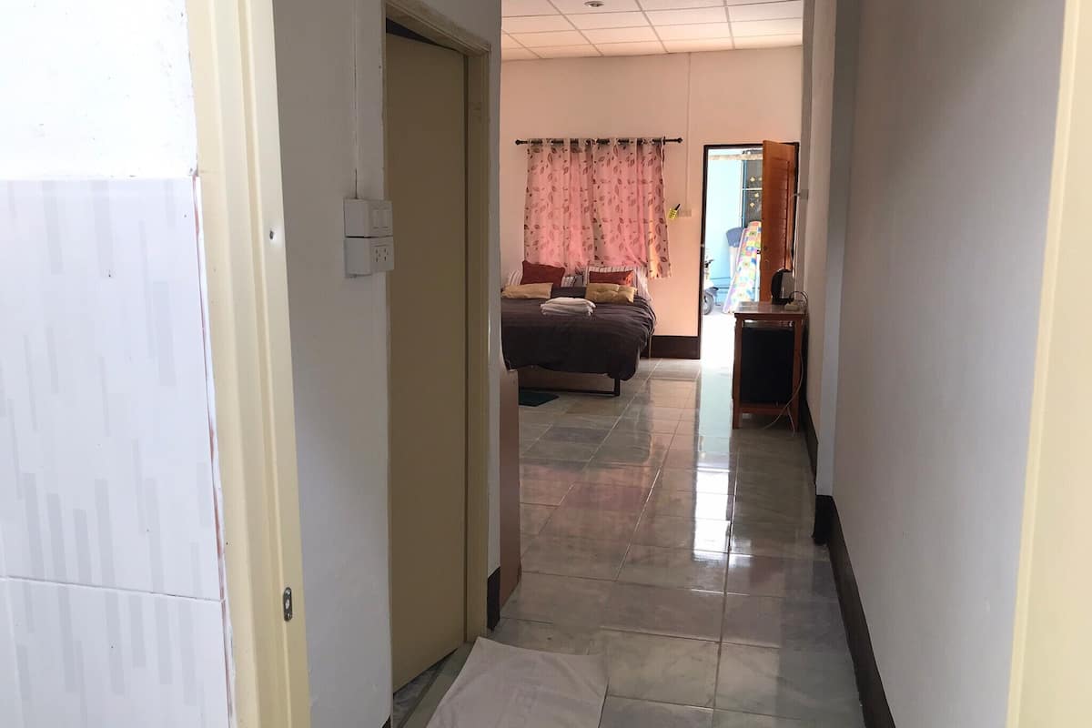 Un couloir menant à une chambre à coucher équipée d’un lit, d’une table de chevet et d’une fenêtre avec des rideaux.