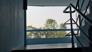Eine Treppe mit Metallgeländer, ein an der Wand befestigter Feuerlöscher und ein Blick auf Bäume sowie ein Gebäude im Freien.