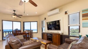 A spacious living room with leather sofas, a wooden coffee table, a ceiling fan, a flat-screen TV, and a large window offering a view of the ocean. - "I have traveled the world and this is the best beach I have ever seen" (La Ribera)