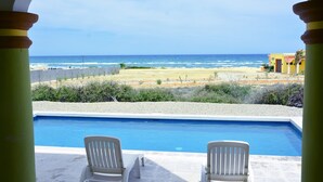 A pool with two white chairs, a view of the beach, and a building in the background. - "I have traveled the world and this is the best beach I have ever seen" (La Ribera)