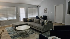Un salon moderne avec un canapé d’angle, une table basse ronde et un coin repas comprenant une table et des chaises.
