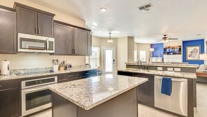 A modern kitchen with dark cabinetry, stainless steel appliances, and a central island. - Spa & Pool + Stay in Harry Potter Theme Home (Frisco)