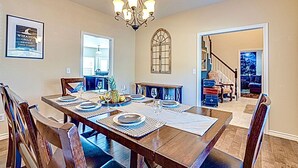 A dining area with a wooden table set for four, a chandelier, and a framed quote on the wall. - Spa & Pool + Stay in Harry Potter Theme Home (Frisco)