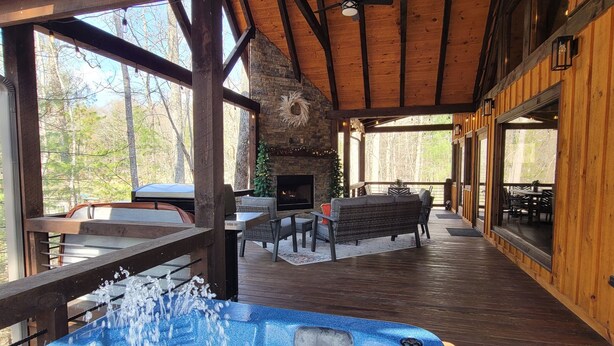 A wooden cabin interior with a hot tub, stone fireplace, and outdoor seating area. - Incredible firepit, luxurious cabin, indoor&outdoor fireplaces. Minutes to town. (Morganton)