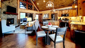 A spacious kitchen with wooden cabinets, a stone fireplace, and a dining area with a round table and chairs. - Incredible firepit, luxurious cabin, indoor&outdoor fireplaces. Minutes to town. (Morganton)