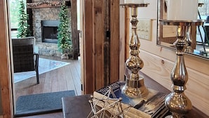 A wooden interior with a fireplace, a dining table with decorative items, and a view of a stone wall and outdoor area. - Incredible firepit, luxurious cabin, indoor&outdoor fireplaces. Minutes to town. (Morganton)